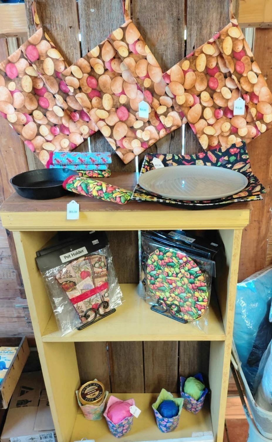 Wooden shelf display with woven fruit baskets, colorful plates, packaged goods, and small jars of candy