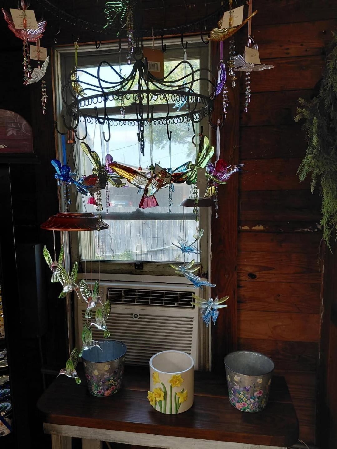 Decorated window with hanging crafts and three small containers on the sill, featuring an air conditioner.