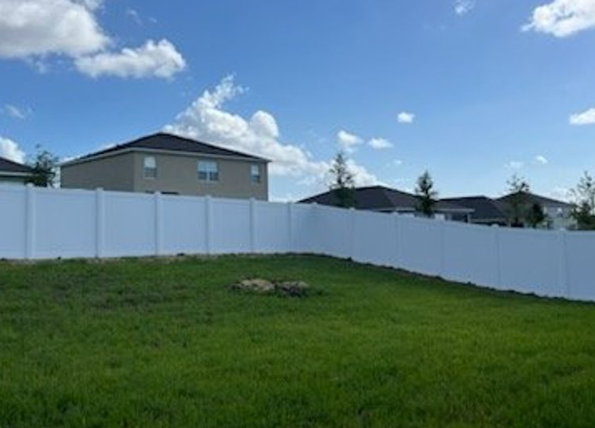A grassy backyard with a white fence, blue sky, and houses in the background.