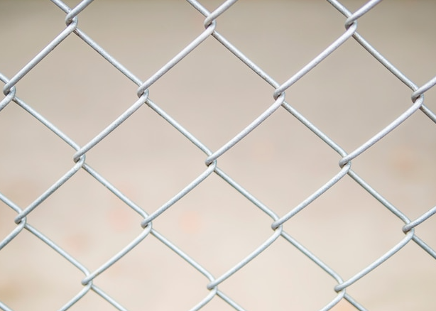 Close-up of chain-link fence, silver metal, with a blurry neutral background.