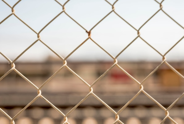 Chain-link fence in focus, blurred background of tracks and buildings.
