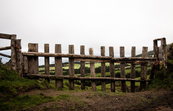 Wooden fence on a grassy hill overlooking a green valley under a cloudy sky.