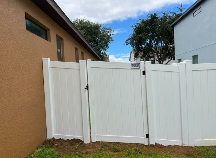White vinyl fence and gate between two buildings on a sunny day.