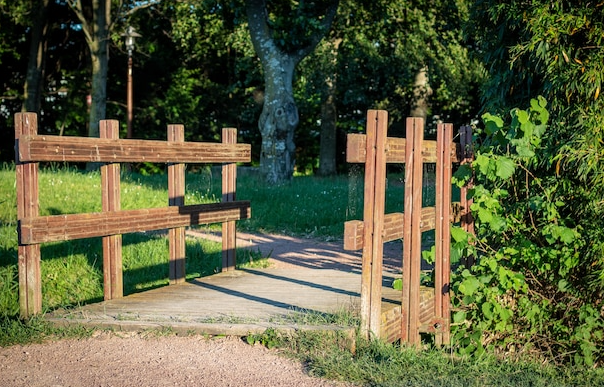 Wooden gate open to a grassy path in a park setting.
