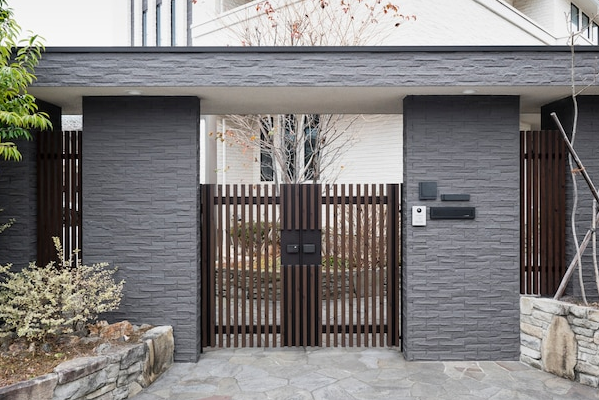 Gray stone entrance gate with brown gate, pillars, and vertical slats.