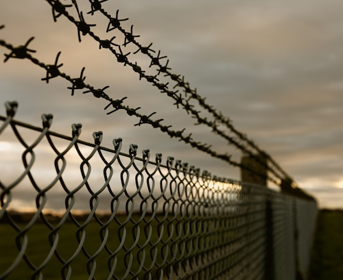 Chain-link fence topped with barbed wire against a cloudy sky; security barrier.