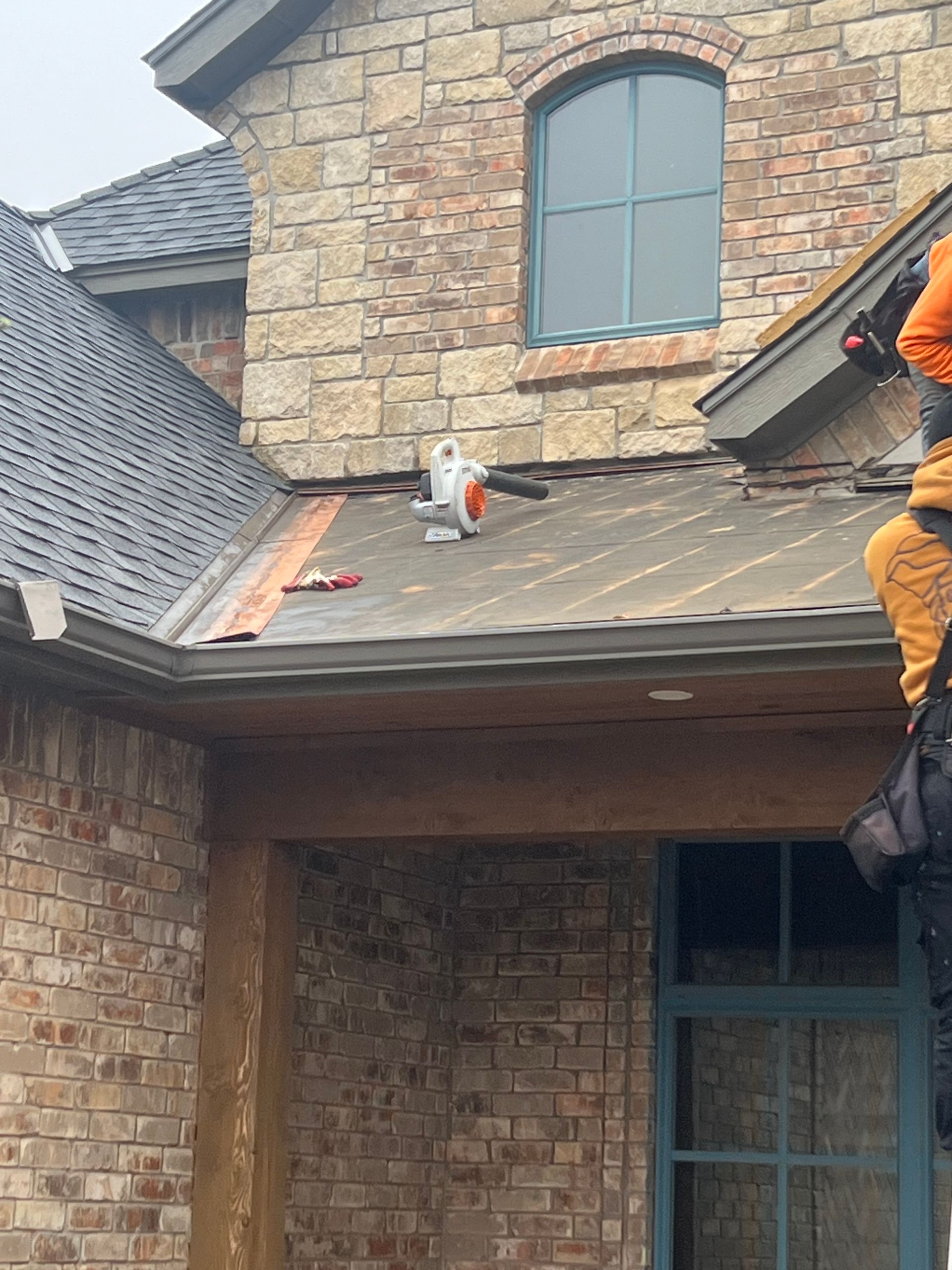 Man on roof uses blower, copper gutter, brick house.