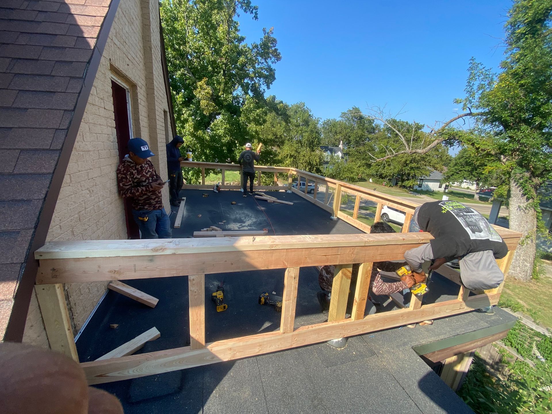 Workers building a wooden railing on a flat roof; sunny day.