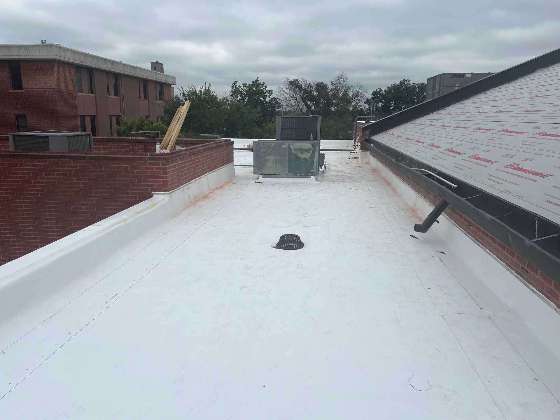 White roof with a brick building and equipment. Cloudy sky.
