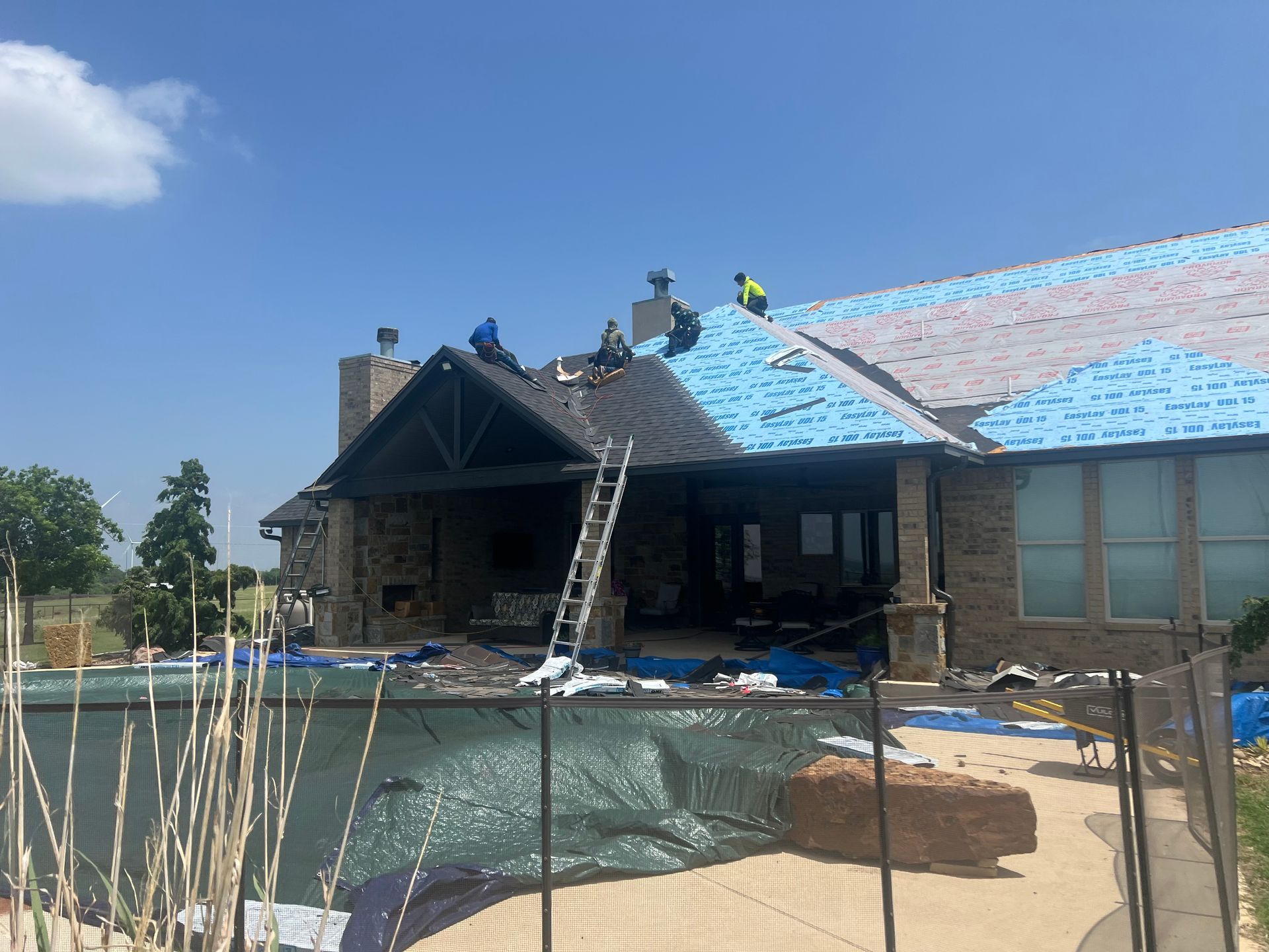 Roofers working on a residential roof; pool and blue tarp in foreground.