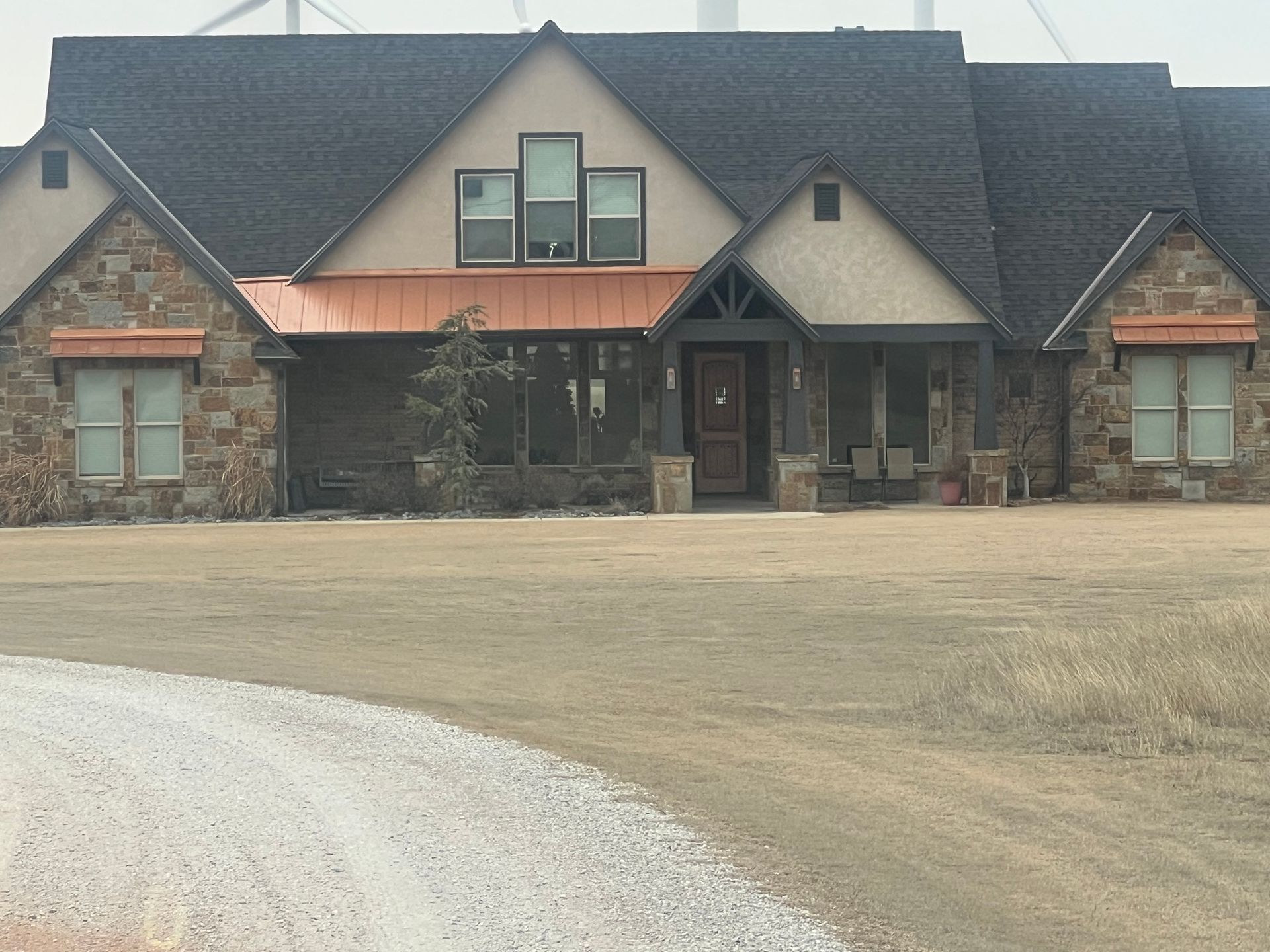 Stone and tan house with copper accents, brown roof, and a gravel driveway.