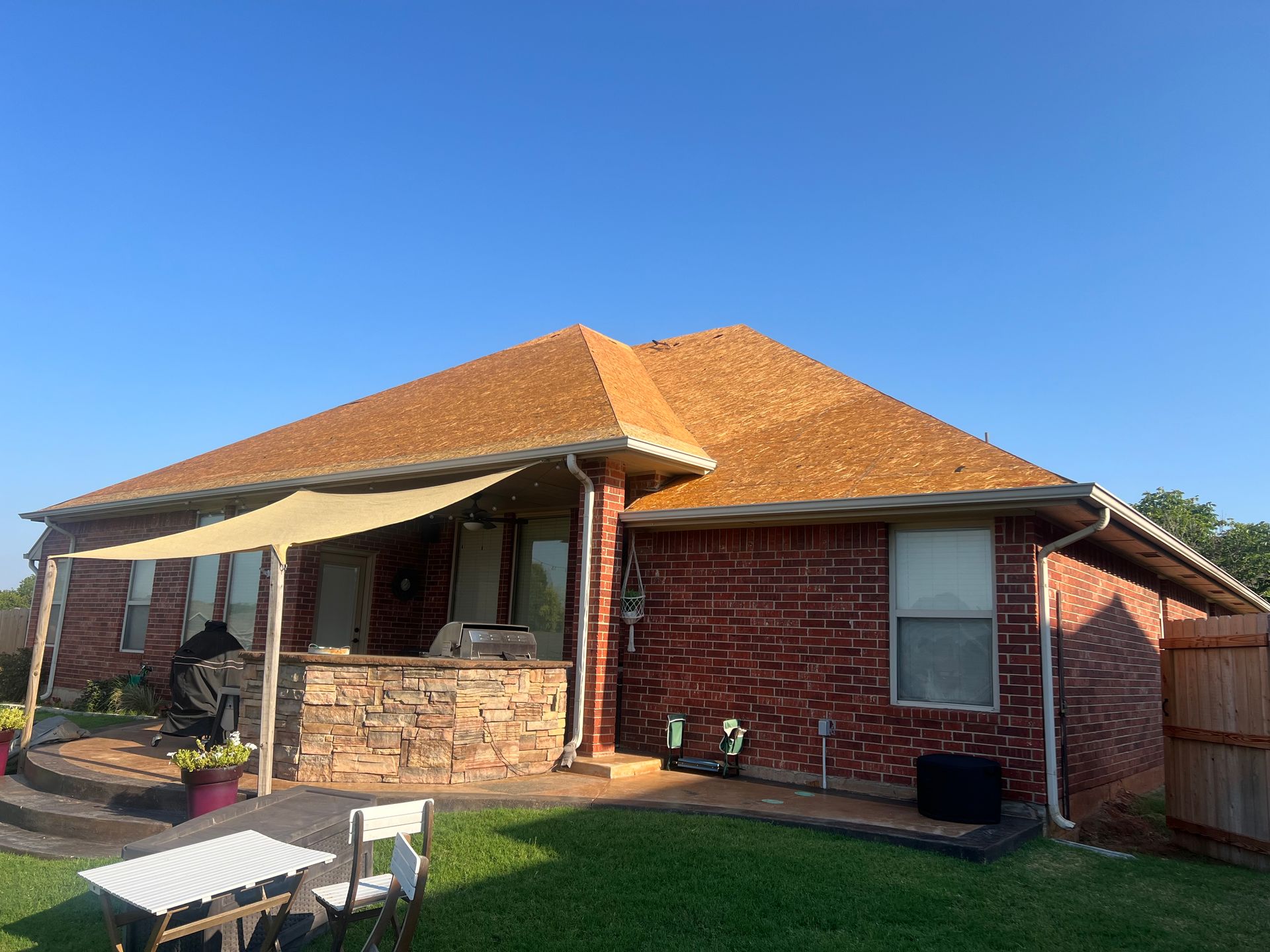 Red brick house with brown roof, back patio, grass, and blue sky.