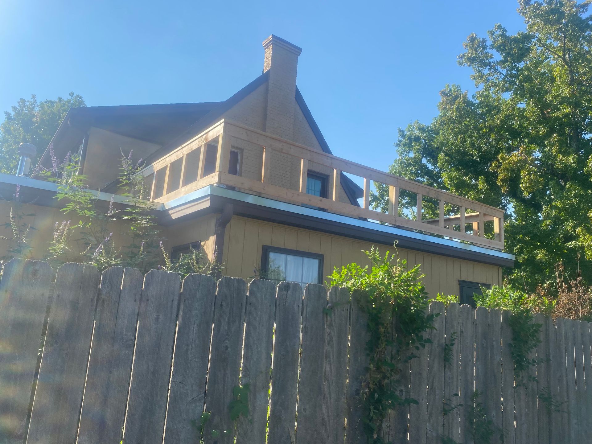 Yellow house with wooden deck and fence on a sunny day.
