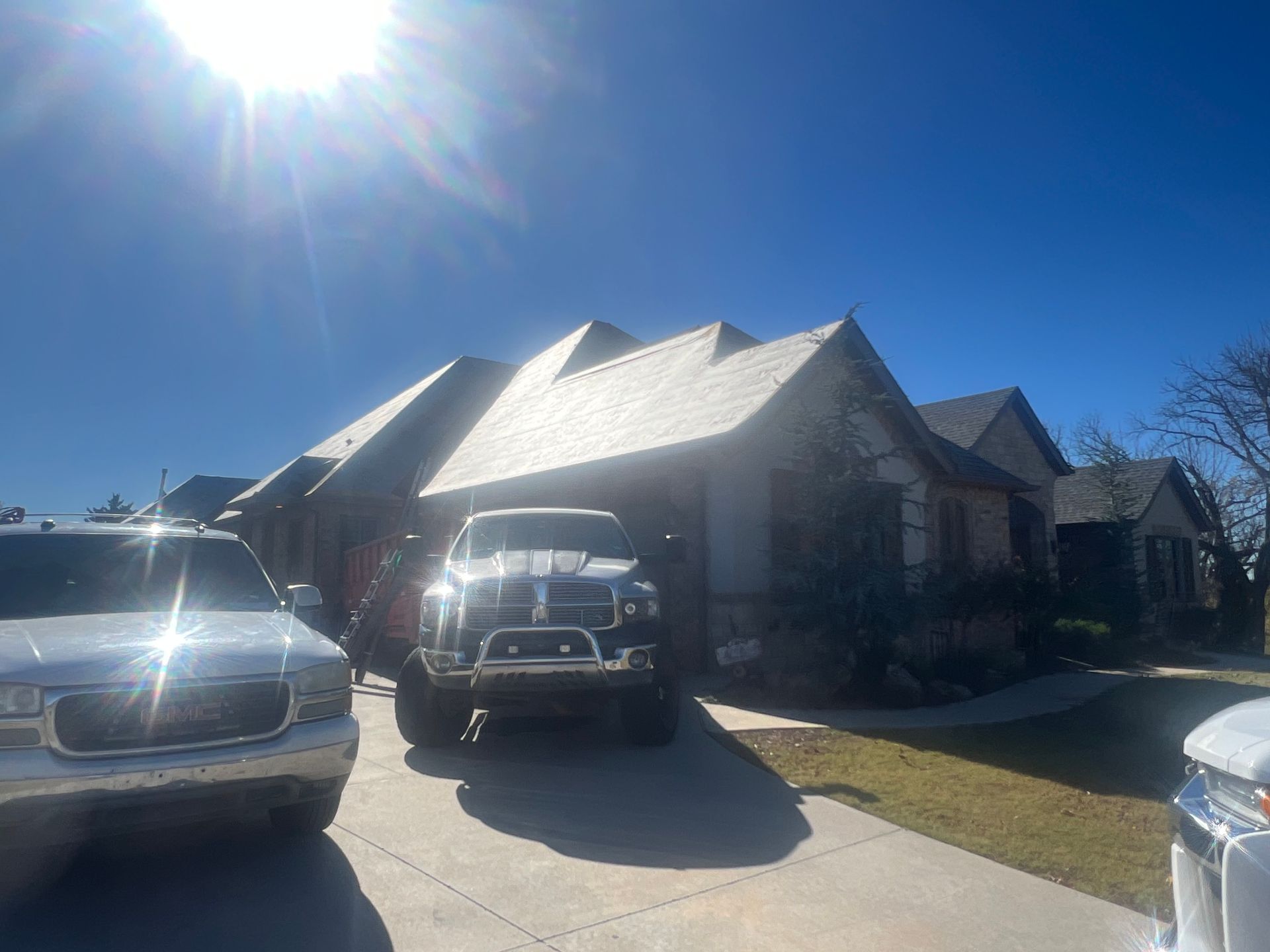 Bright sun over a house with a dark truck parked in the garage and a white truck on the driveway.