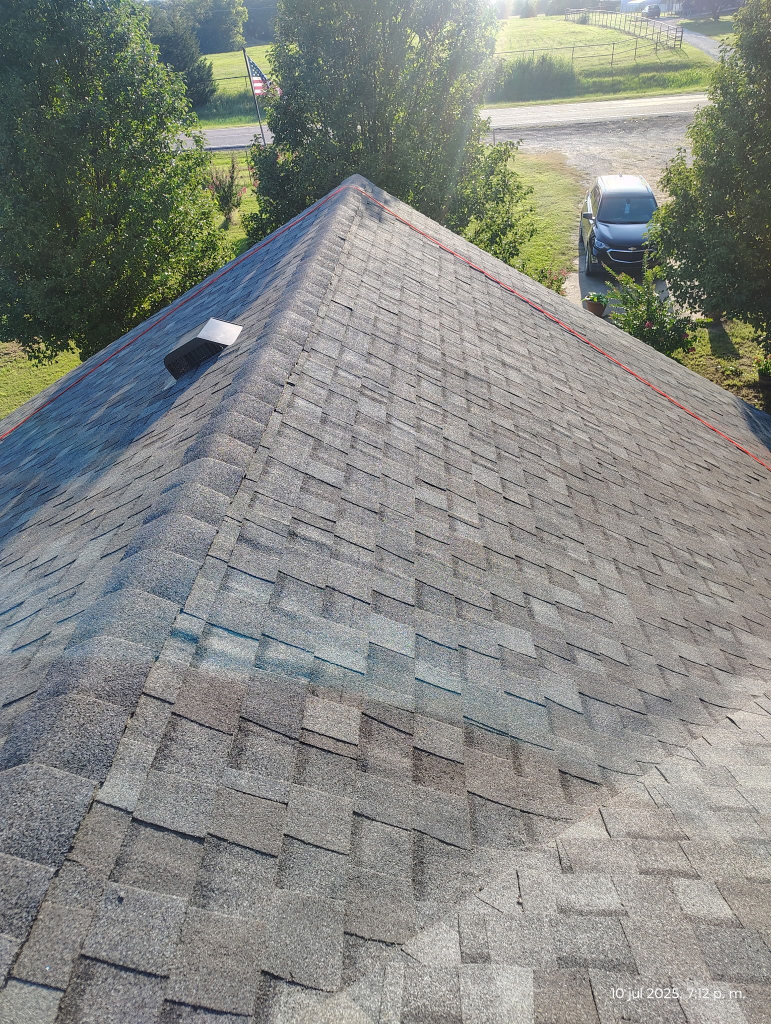 Overhead view of a weathered gray shingle roof on a building with a car in the background on a sunny day.