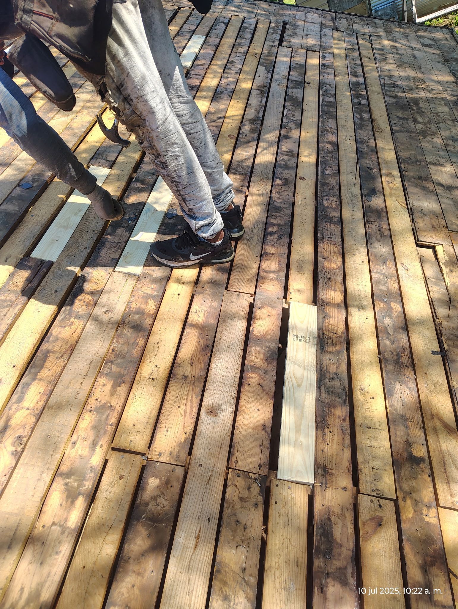 Person standing on wooden pallets, building construction, outdoors, sunlight.