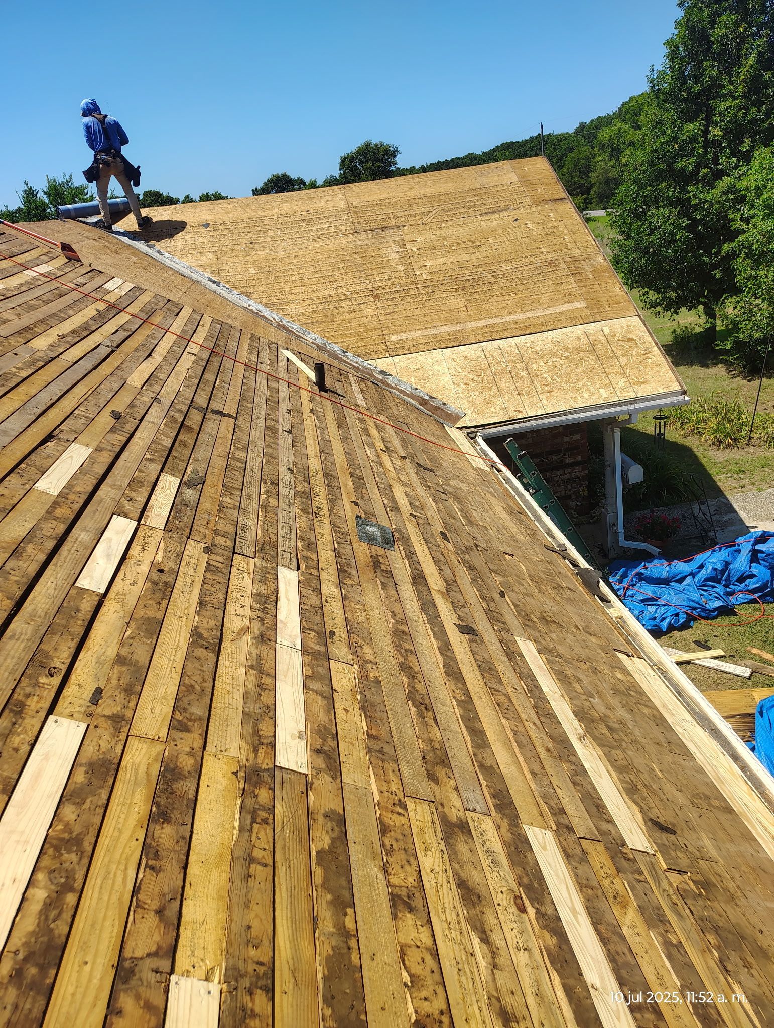 Roofer working on a partially shingled roof. Sunny day with clear blue sky.