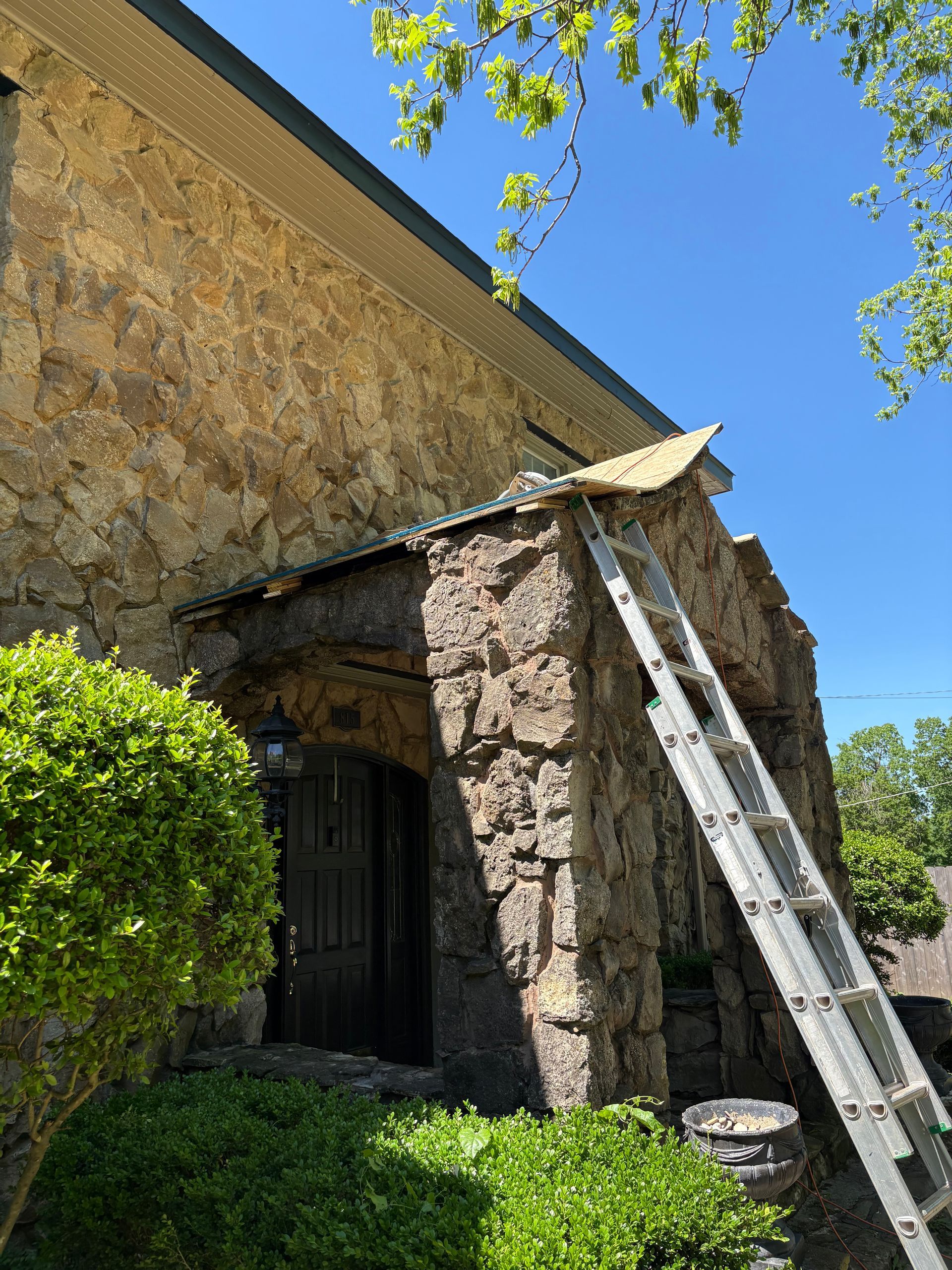 Stone building entrance with a ladder leaning against it; sunny day.