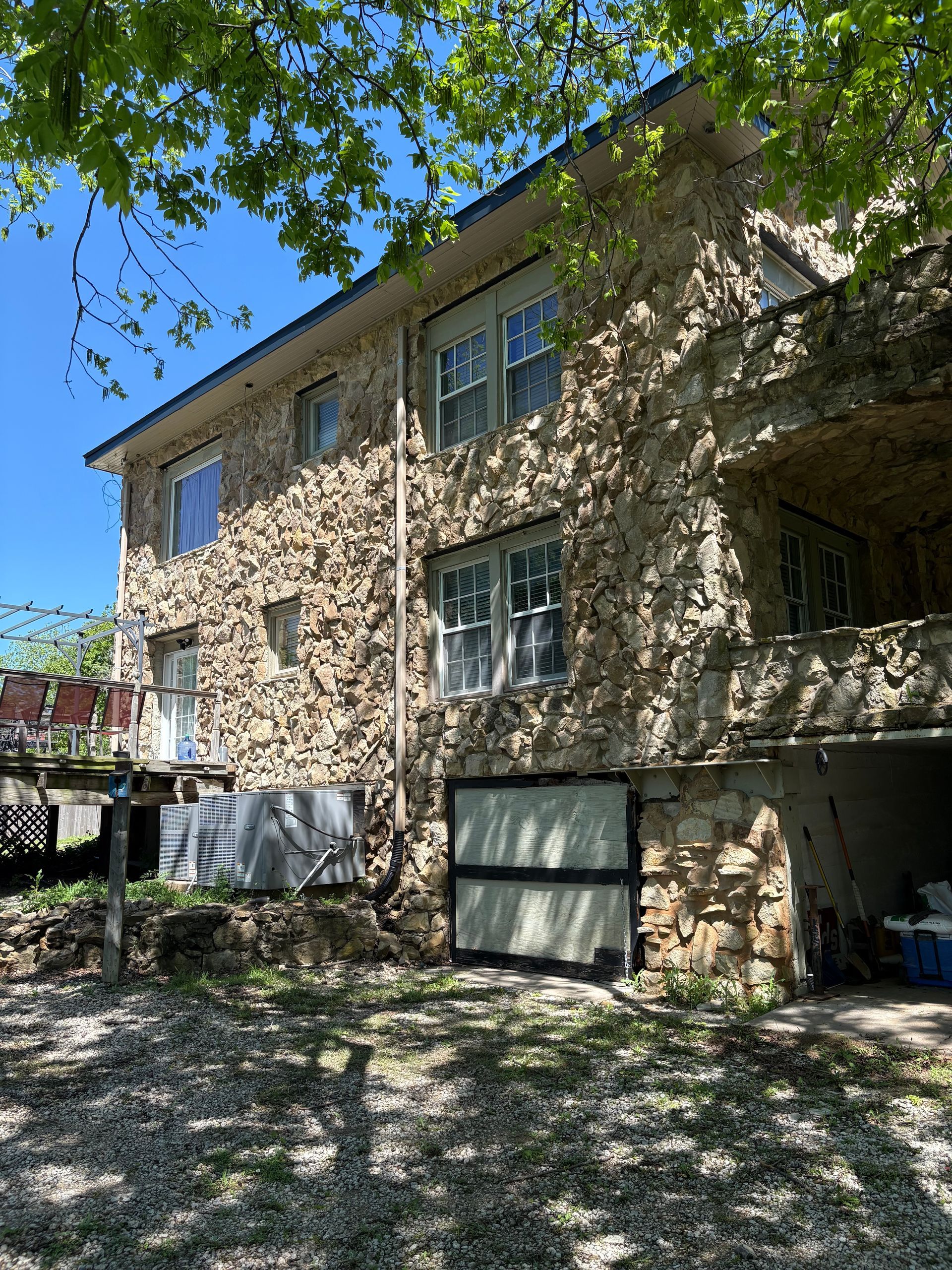 Two-story stone house with open garage. Overcast and sunny. Trees overhead.