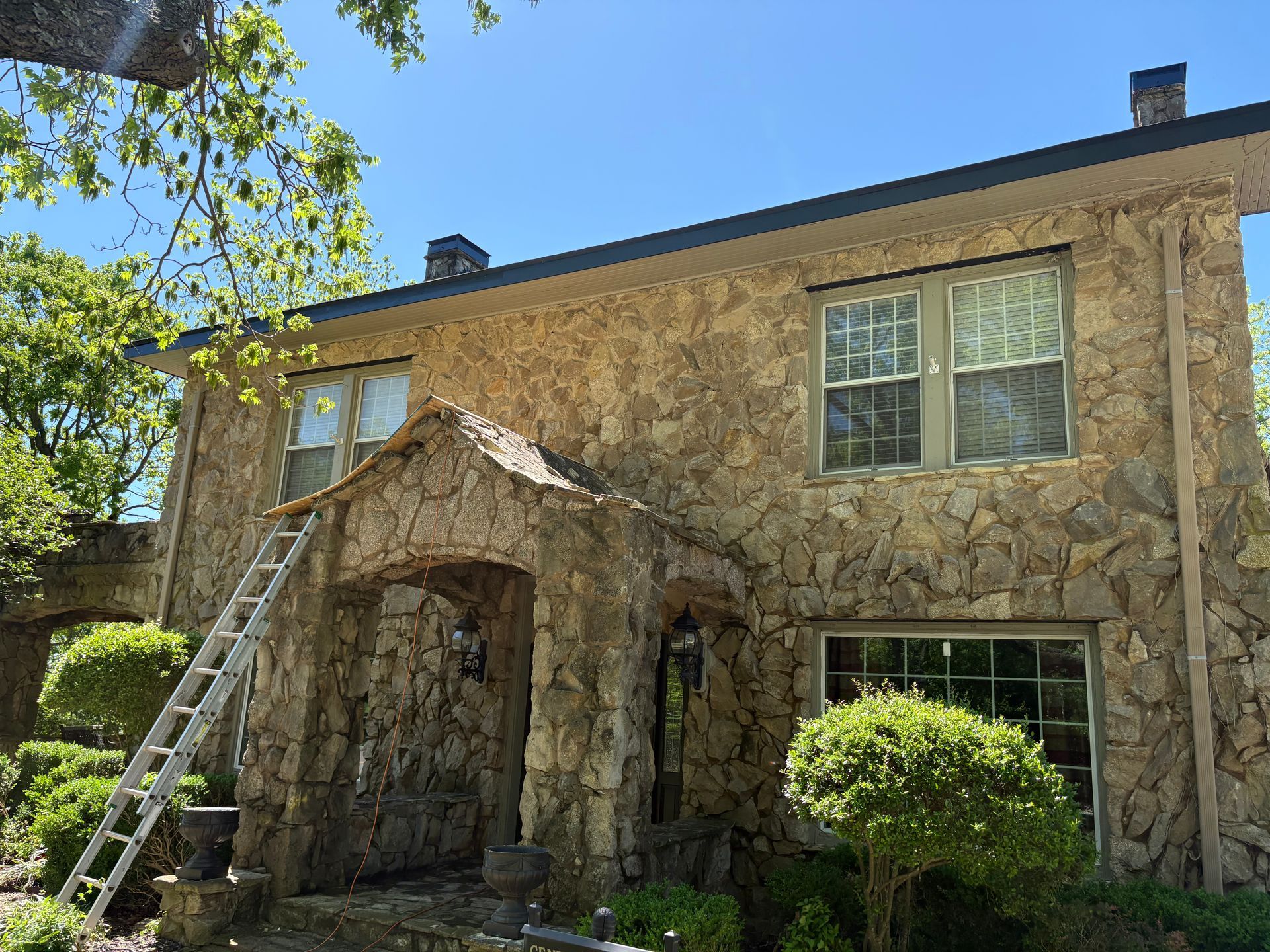 Stone house with a ladder leaning against it on a sunny day.