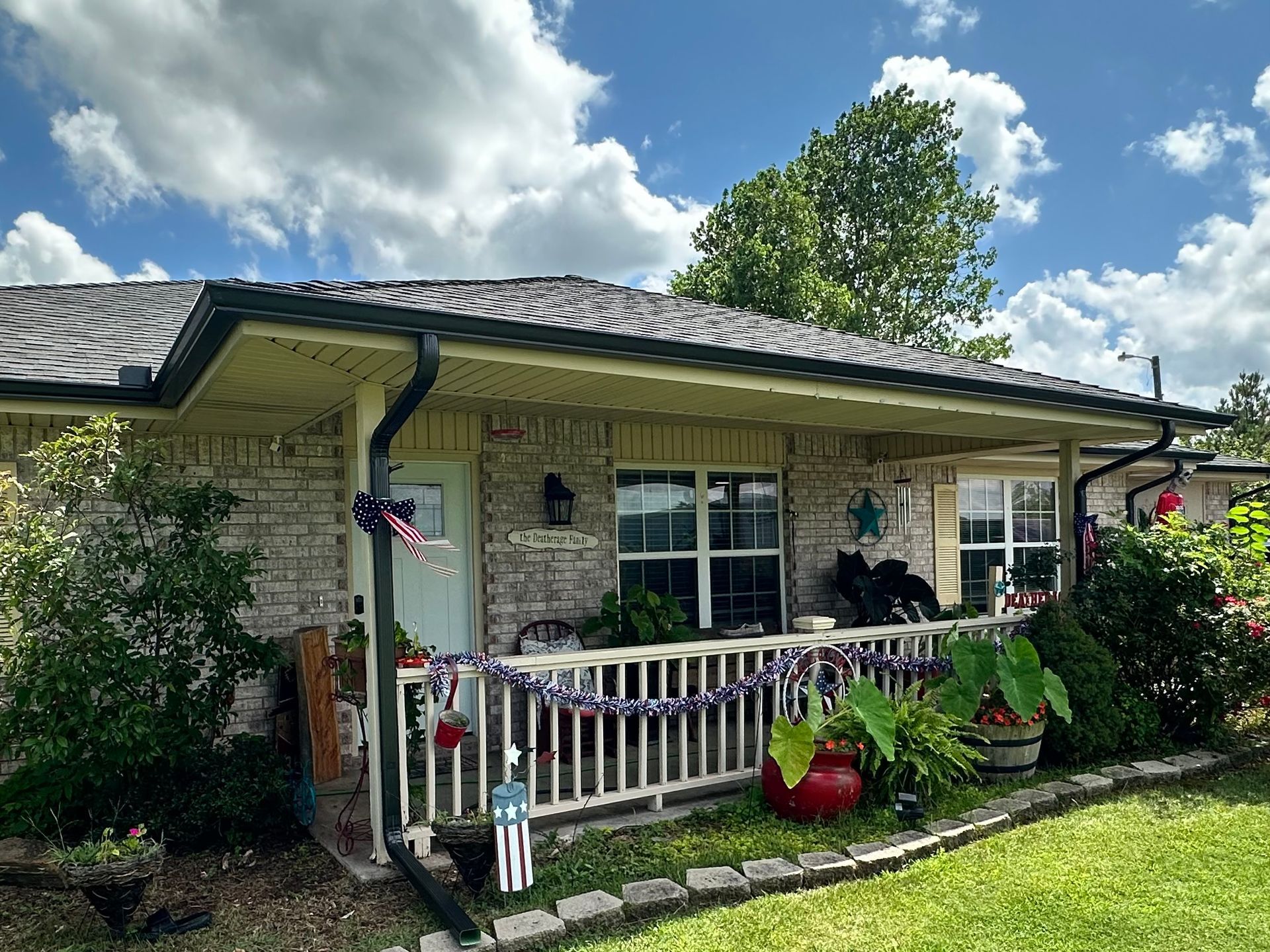 Brick house with porch decorated with patriotic colors under a cloudy blue sky.