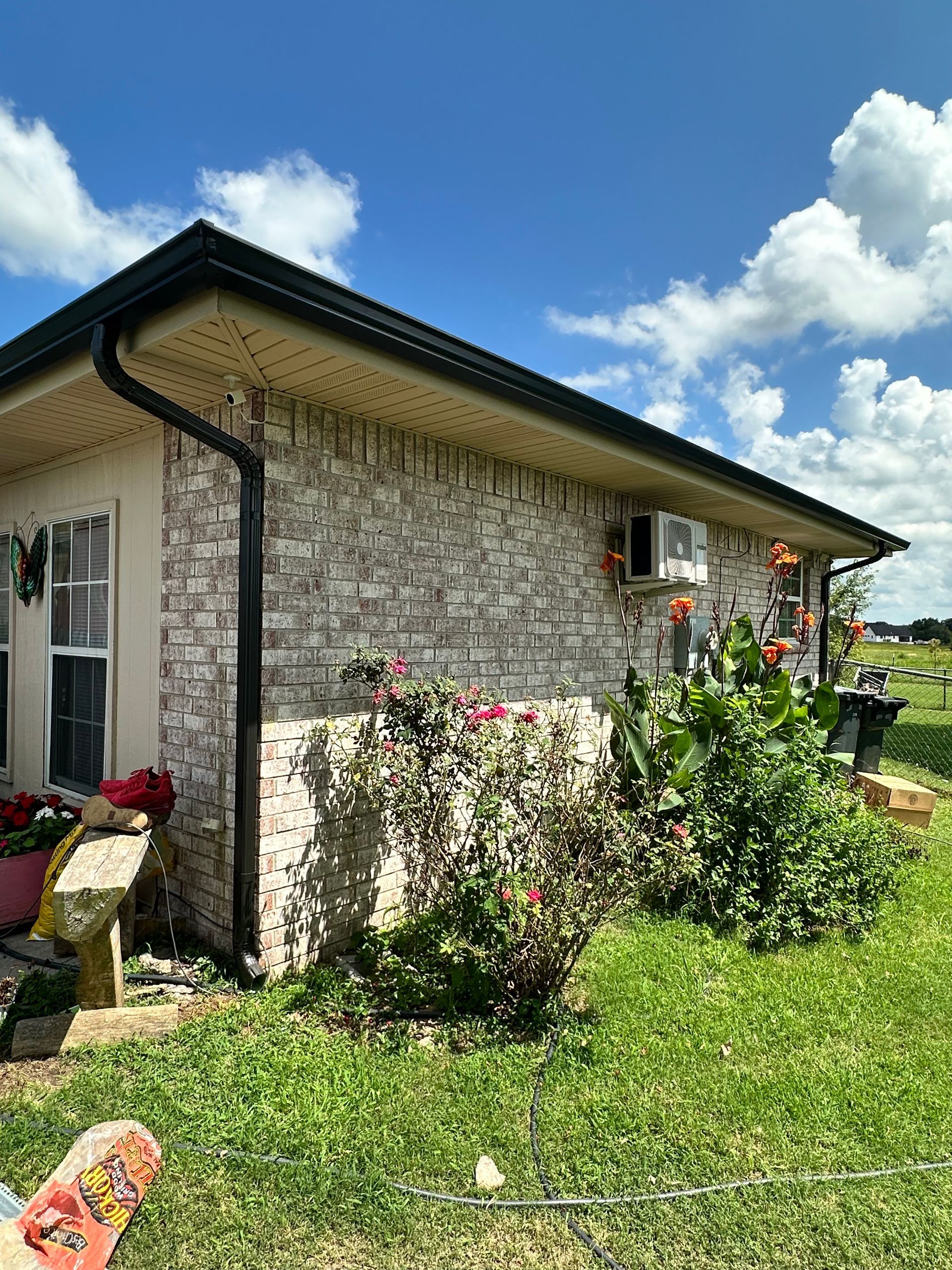 Brick house with black gutters, surrounded by greenery and a cloudy sky.
