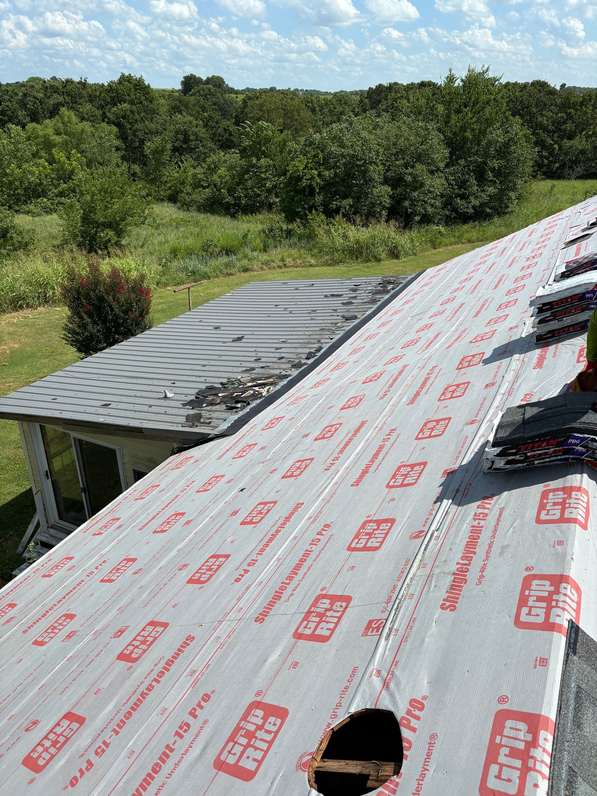 Roof being repaired, showing new underlayment and hole, with trees and sky in the background.