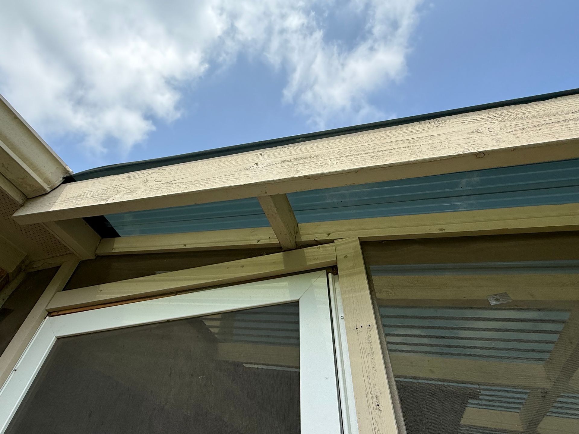 A close-up view of a building's exterior with a window, blue siding, and tan trim against a partly cloudy sky.