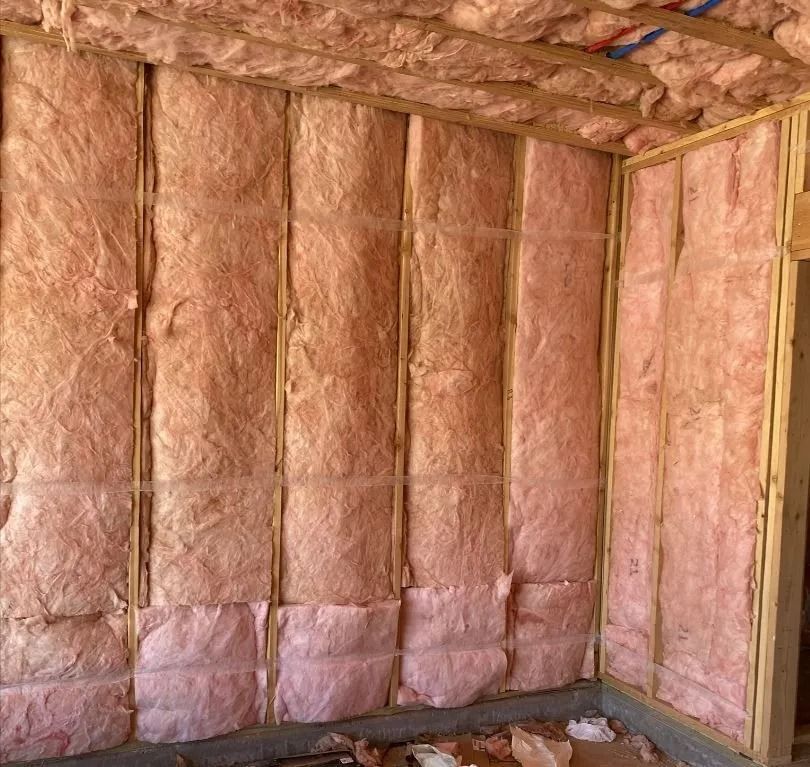 Pink fiberglass insulation installed between wooden wall studs of a room under construction.