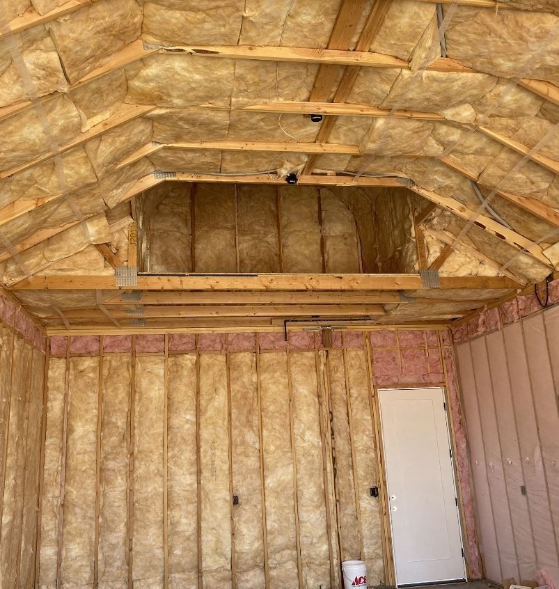 Interior of a building under construction, showing insulation on walls and ceiling, a door, and an open alcove.