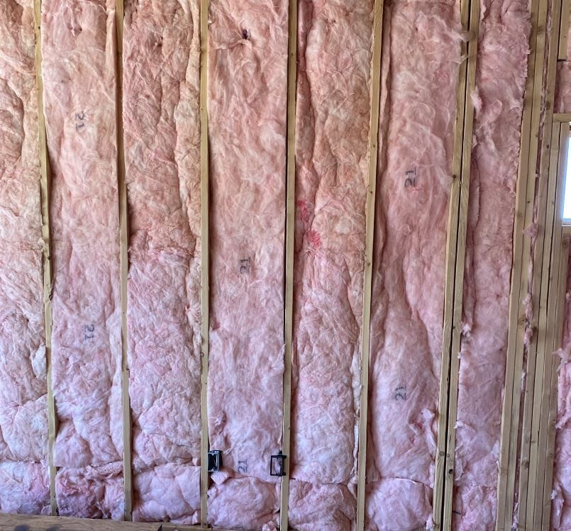 Pink insulation batts between wooden wall studs in a building under construction.