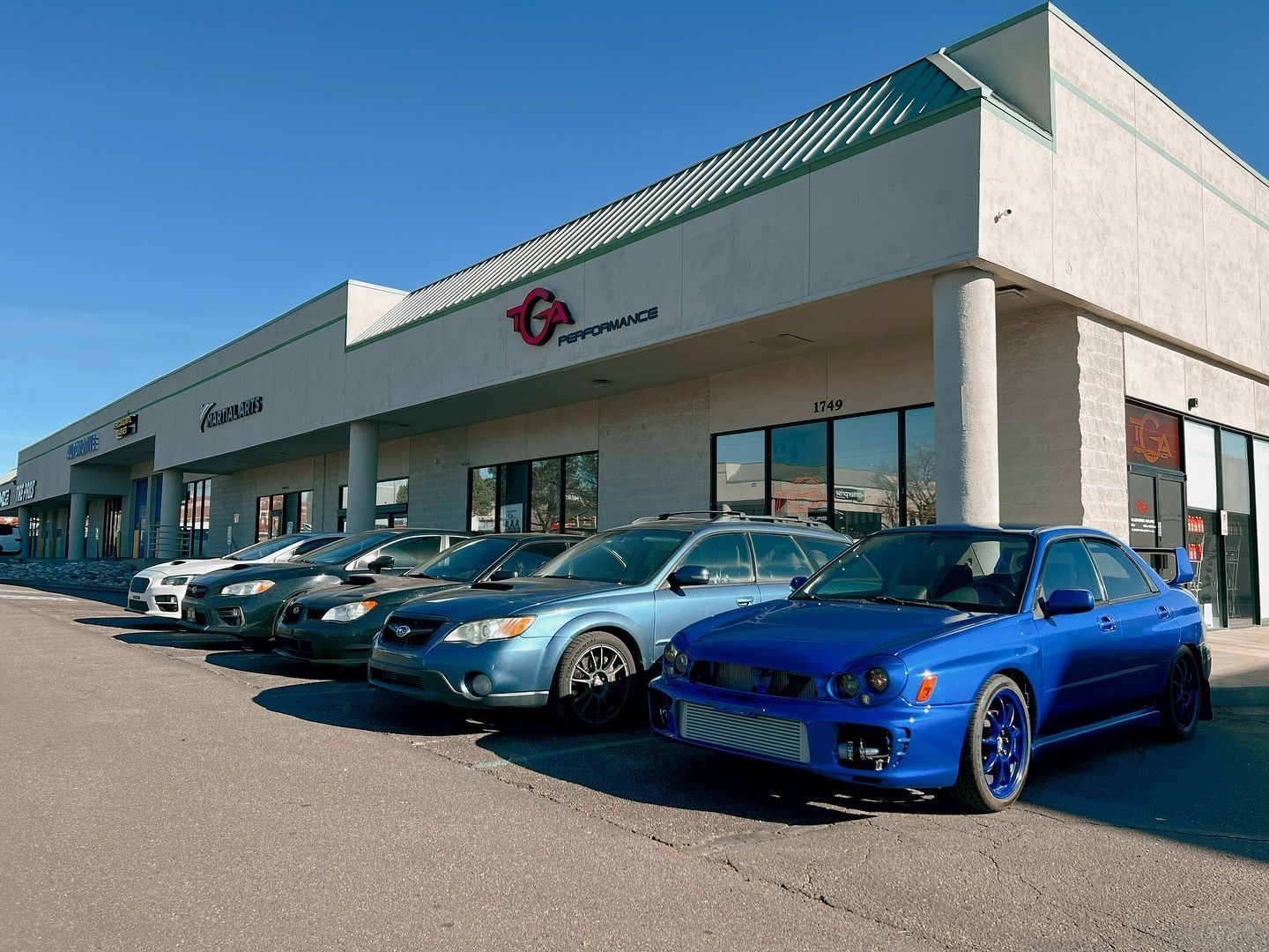 A row of cars are parked in front of a car dealership