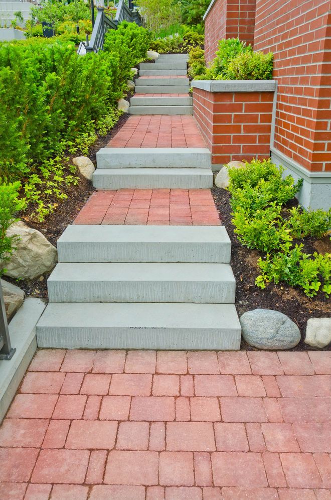 Brick and concrete outdoor staircase between landscaped shrubs and a red brick wall