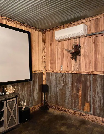 Rustic home theater with wood paneling, corrugated metal ceiling, projector screen, and air conditioner.