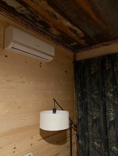 Air conditioner unit on wooden wall above lamp and camouflage curtain.