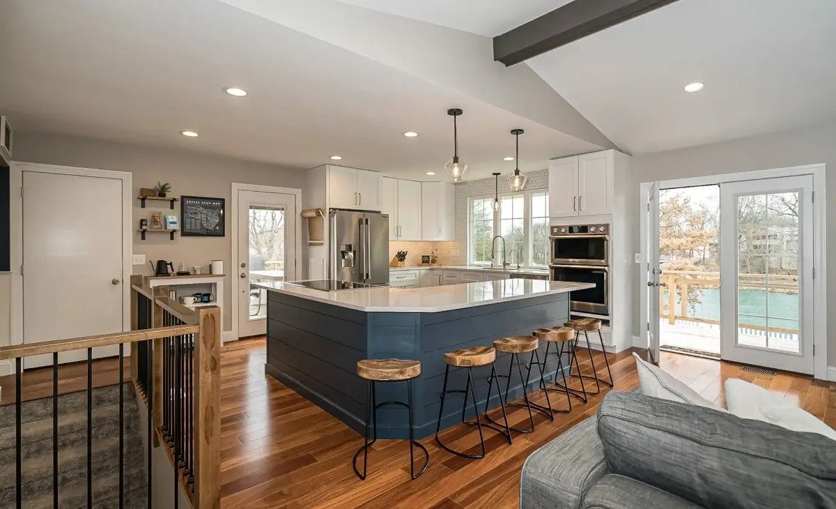 Modern kitchen with blue island, white cabinets, and wood flooring; bright, airy space with outdoor view.