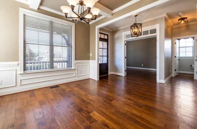 Empty dining room with hardwood floors, tan walls, large window, and chandelier.