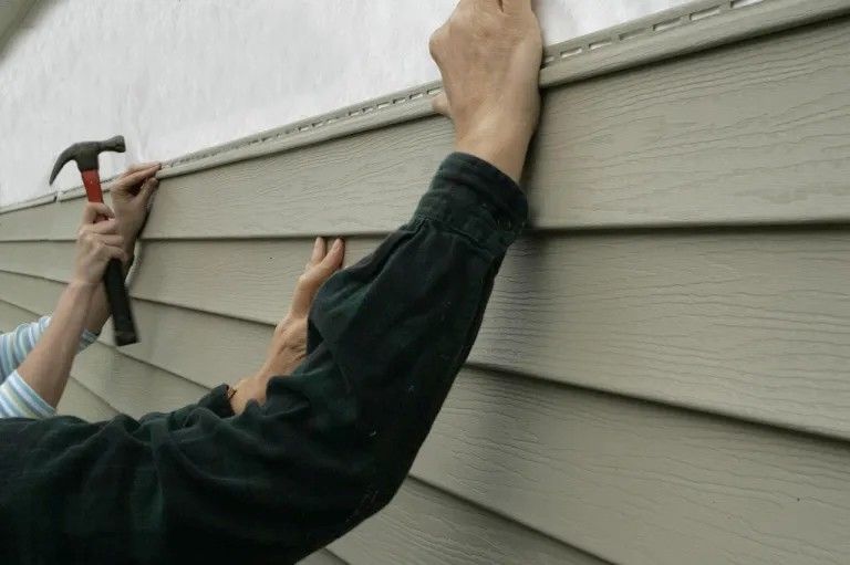 Person hammering tan vinyl siding onto a wall.
