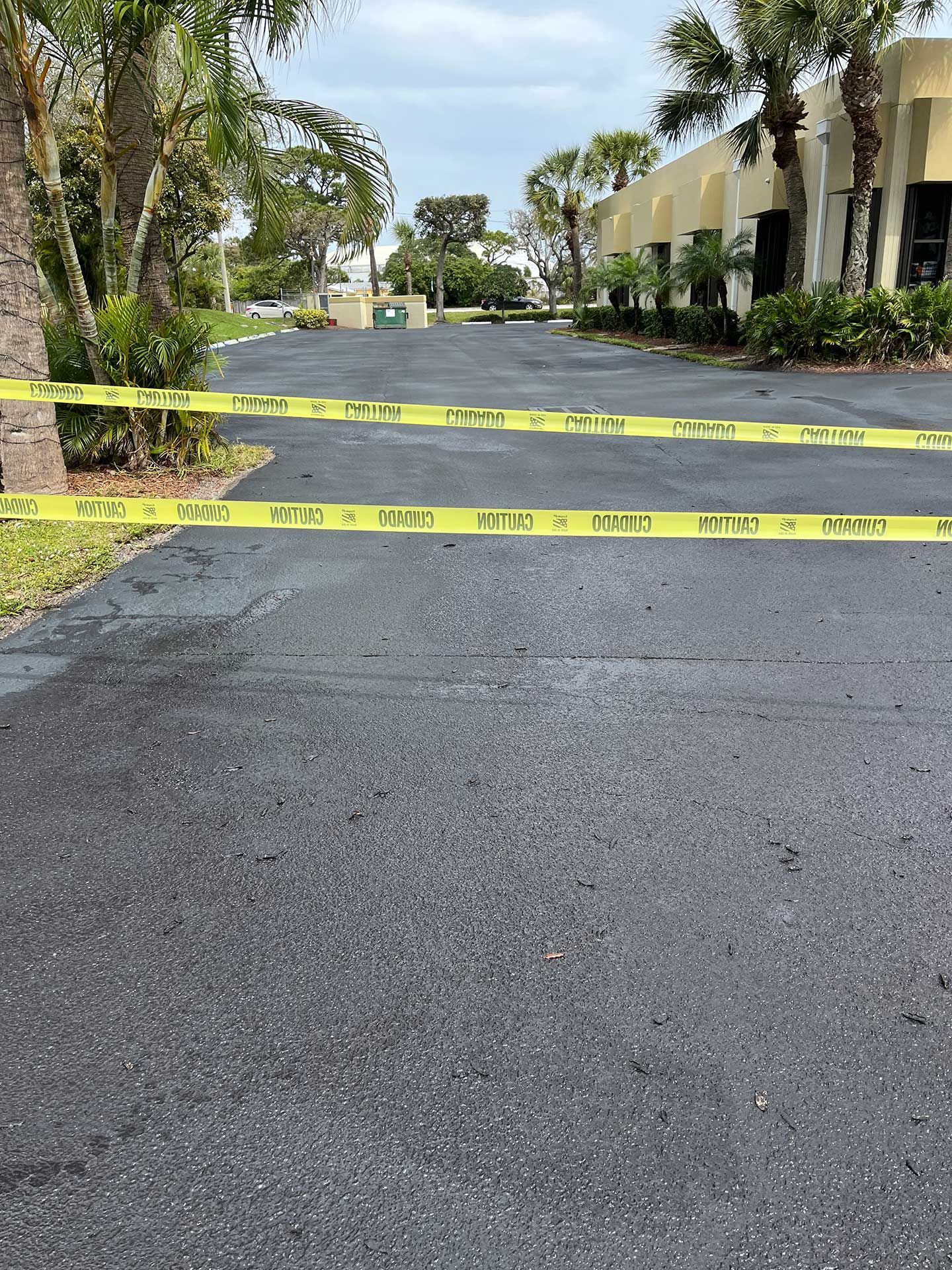 a paved driveway with yellow tape on it and a building in the background
