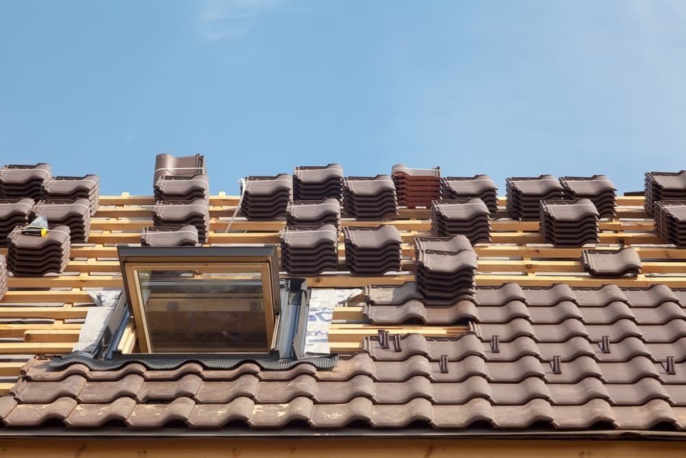 Roof with brown tiles being installed, skylight visible, blue sky background.