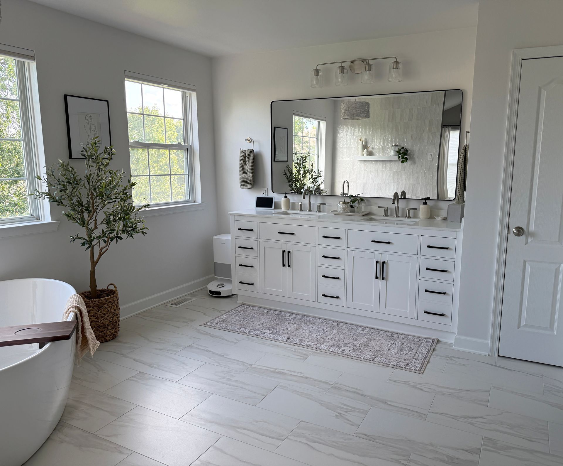 Bright white bathroom with double vanity, large mirror, window, and a freestanding tub.