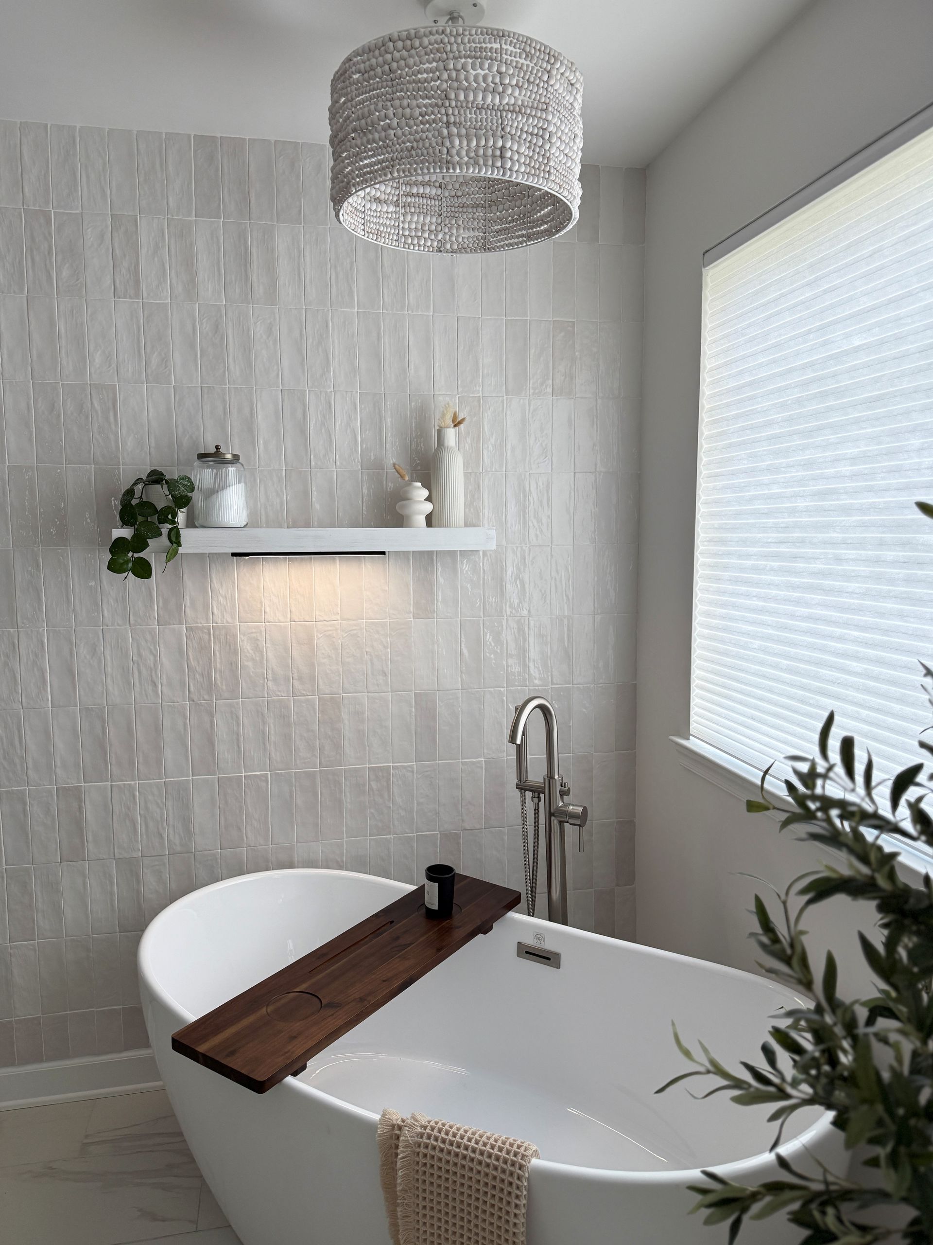 Modern bathroom with a freestanding tub, wooden bath tray, white textured wall, and pendant light
