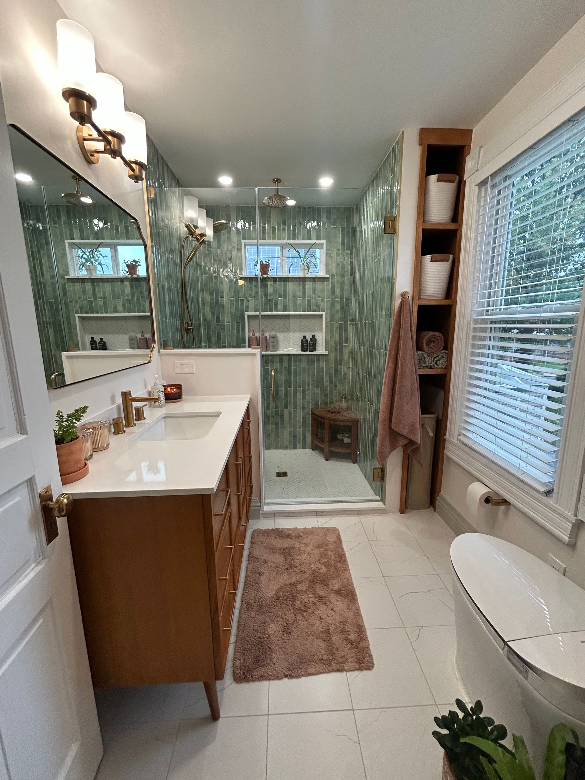 Small bathroom with green tile shower, white vanity, window, and towel rug.