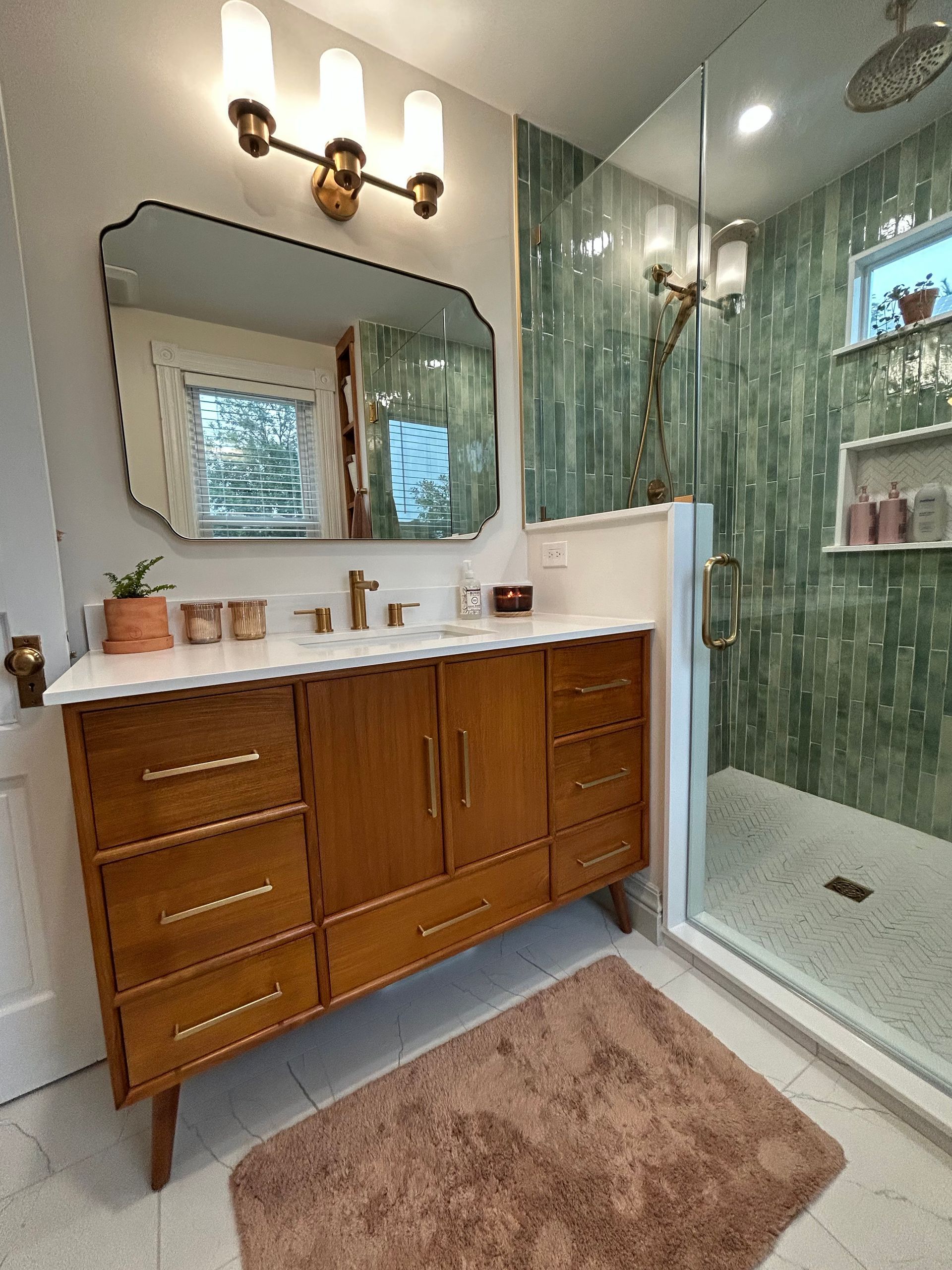 Modern bathroom with wood vanity, large mirror, glass shower, and brown rug