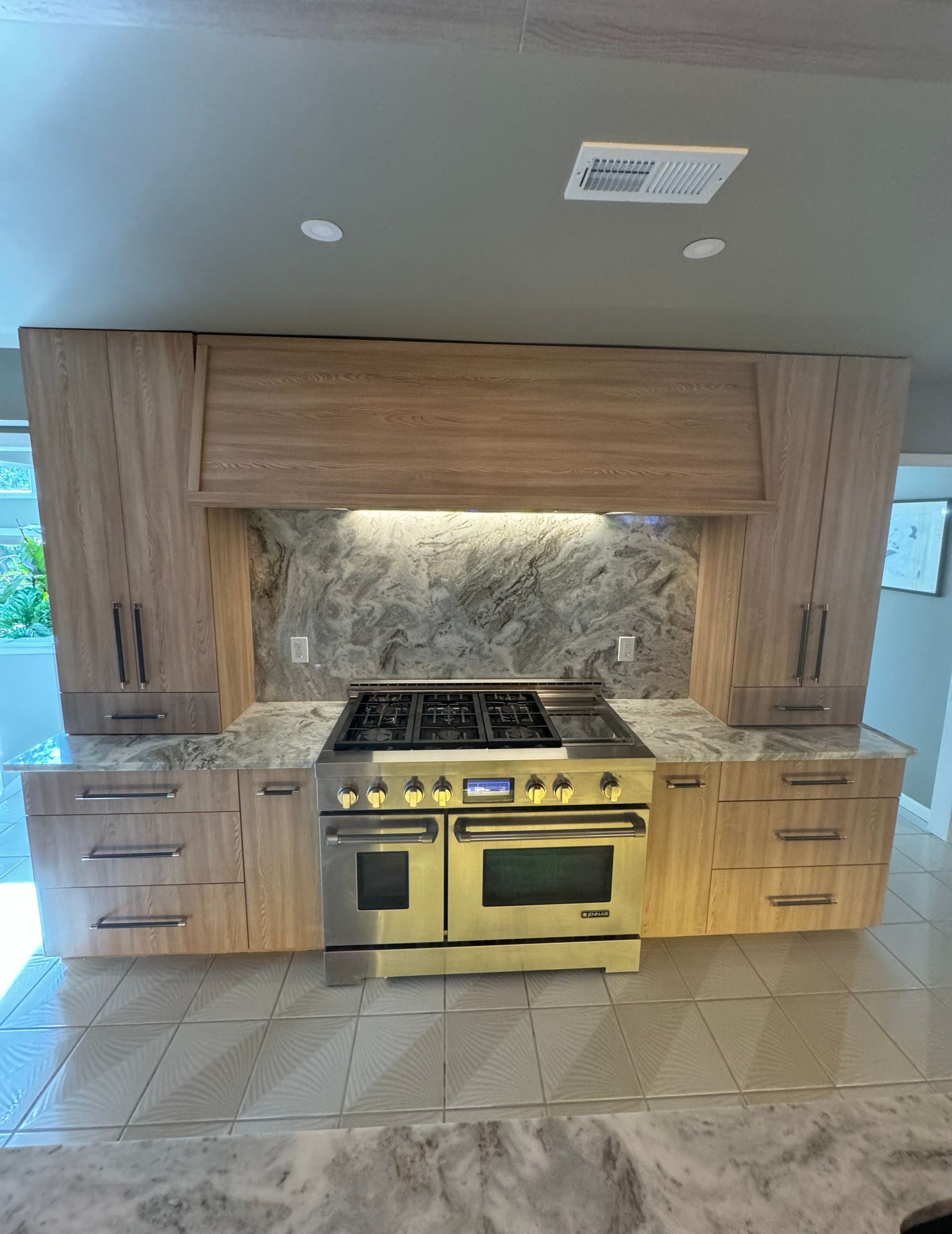 Modern kitchen with wood cabinets, a stainless steel stove, and tiled floor under a recessed-lit hood.