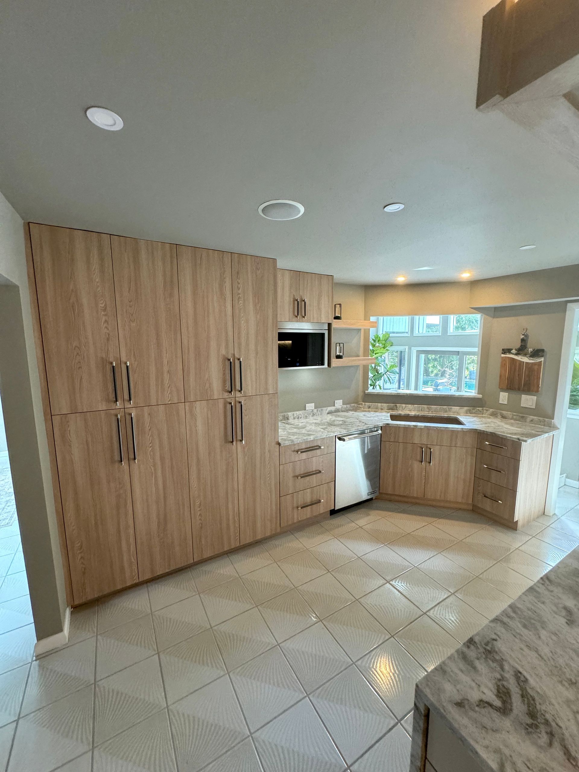 Bright kitchen with wood cabinets, white tile floor, and a window over the sink.