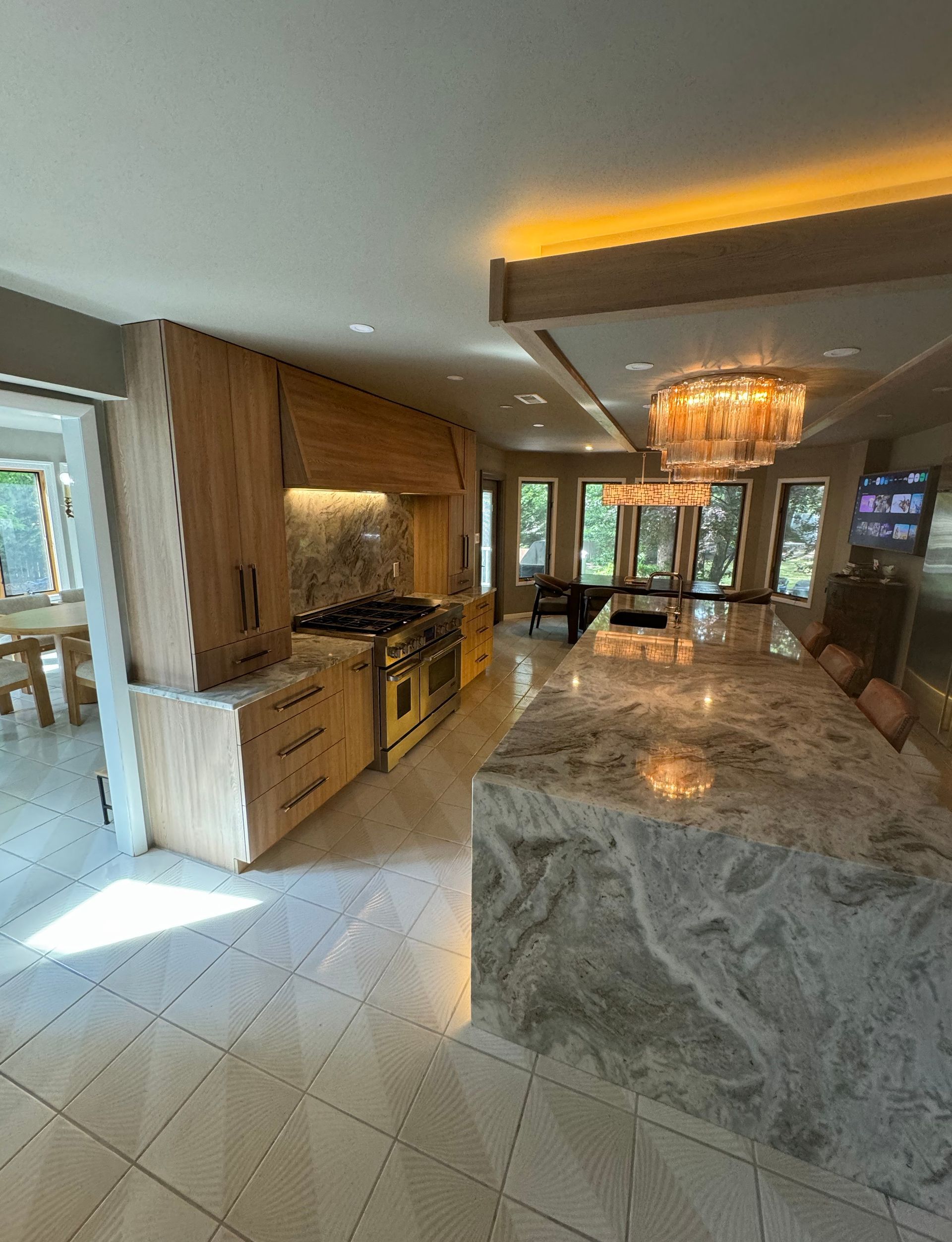 Modern kitchen with marble island, wood cabinets, tiled floor, and warm ceiling lights.