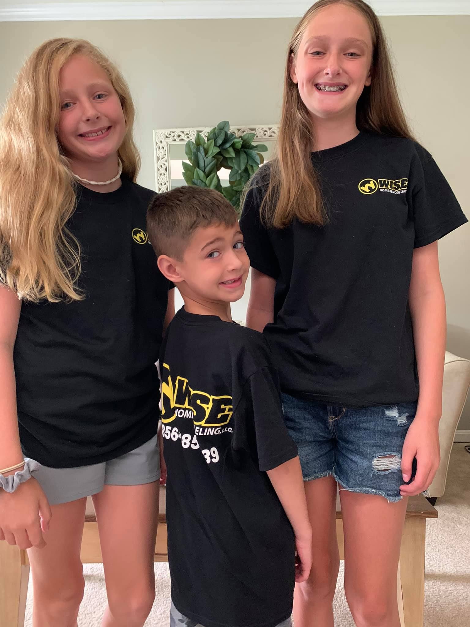 A boy and two girls are standing next to each other in a living room.