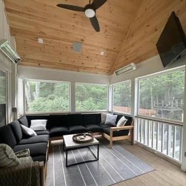 There is a ceiling fan in the living room with a lot of windows.