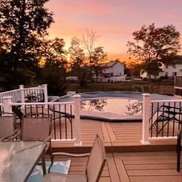 A deck with a table and chairs and a pool at sunset.